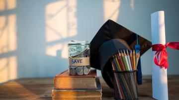 Jar with money on top of two books. To their right is a graduation cap, a container with pencils, and a diploma.